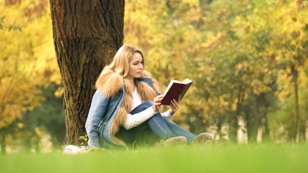 istock Pretty woman reading interesting book, sitting under tree, spending leisure time 1137646213