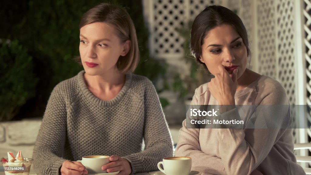 Two upset female friends sitting in cafe, relations conflict, misunderstanding Arguing Stock Photo