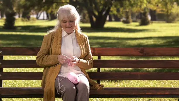 Dreamy old woman knitting little socks for her granddaughter, family generations