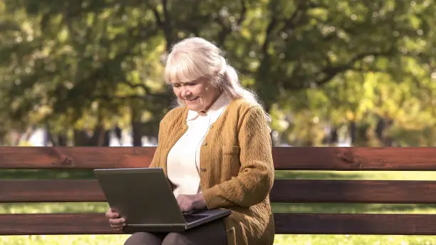 Senior lady working on laptop computer outdoors in park, information technology