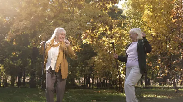 Funny senior women enjoying weather, dancing and having fun in warm autumn park