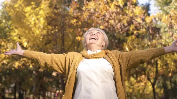 Cheerful granny enjoying beautiful autumn weather strolling in park, golden age