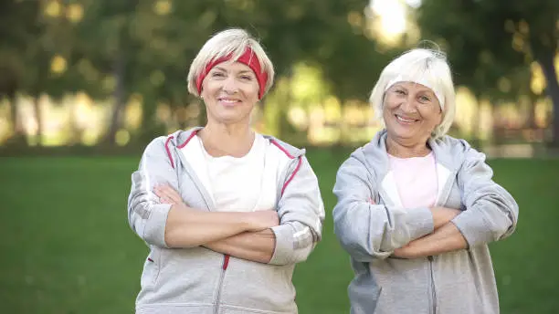 Smiling full of energy mature women posing in park after workout, fitness