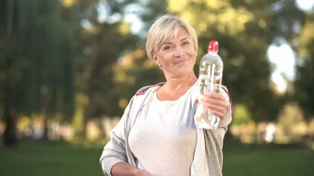 Smiling woman showing bottle of sparkling water before camera, healthy lifestyle