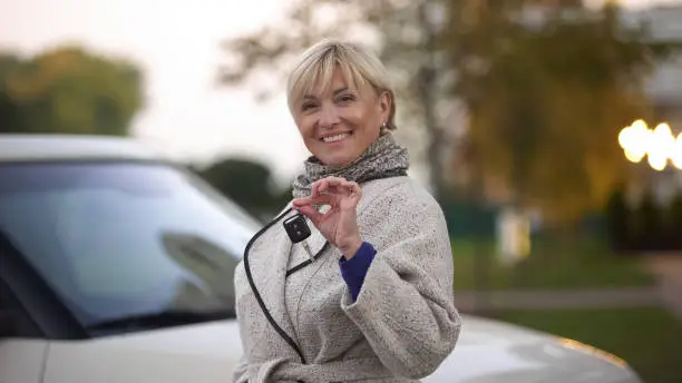 Mature successful woman smiling and holding keys of new luxury car, present