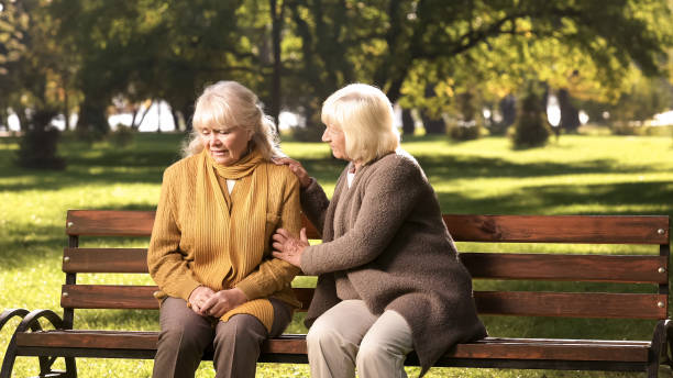 公園でベンチに座って、彼女の損失についての古い友人を慰めるシニアレディ - old senior adult women tired ストックフォトと画像