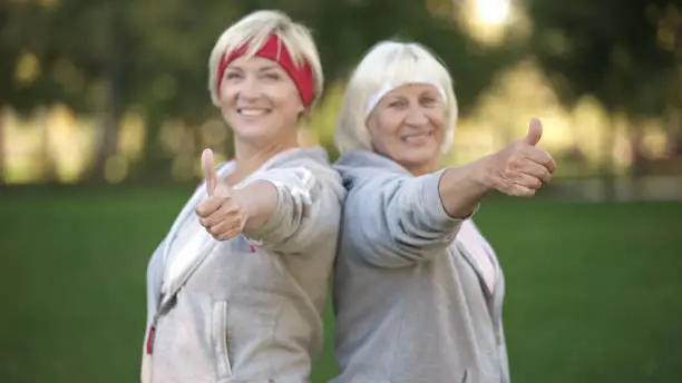 Two happy mature women smiling and showing thumbs up in park, healthy lifestyle