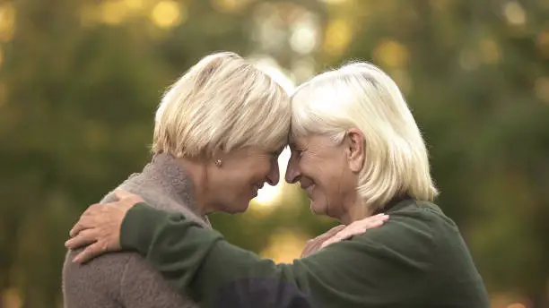 Two mature female friends tightly hugging each other and smiling, happy meeting