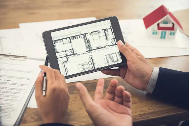 Photo of Real estate agent presenting floor plan to customer on tablet computer