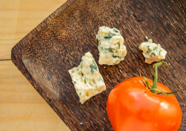 Wooden plate with tomato and cheese with mold. Flat lay top view