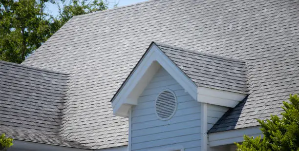 Photo of garret house and Roof shingles on top of the house among a lot of trees. dark asphalt tiles on the roof background