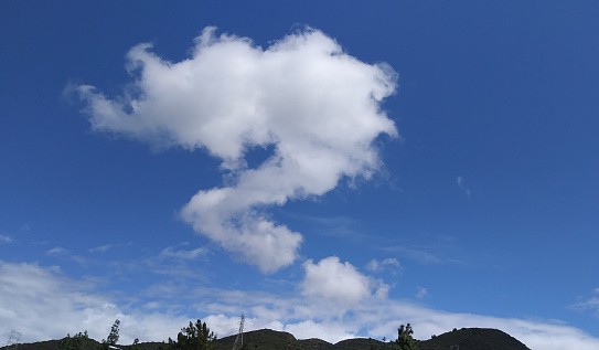 A snapshot of cumulus clouds oddly shaped like a punctuation mark above a group of hills in San Fernando Valley, California.