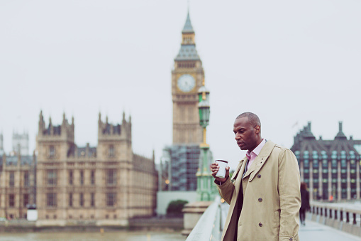 London, Businessman, Confidence, England -  Business Executive holding a cup of coffee lost in thoughts standing at the Westminster Bridge, London