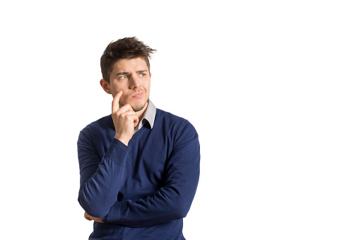 Young thoughtful man in blue sweater and shirt posing on white background