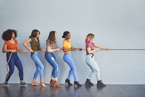 Studio shot of a group of young women playing tug of war against a gray background