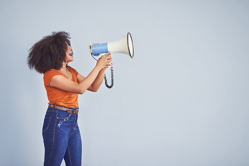 Studio shot of a young woman using a megaphone against a gray background
