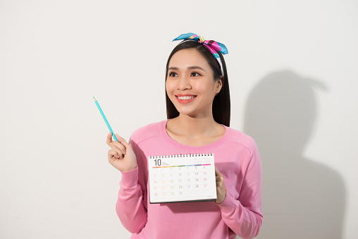 Portrait of a happy cute girl holding her periods calendar with a pen and looking away at copy space isolated over white background