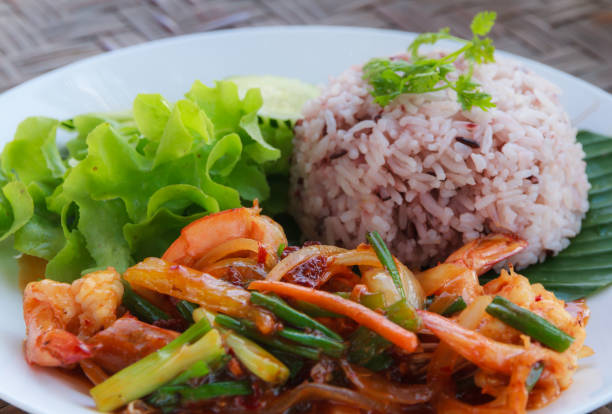 stir fried shrimp in thai red curry paste with rice and green vegetable , Spicy Fried Shrimp , Curry fried shrimps and cooked rice in white dish closeup on table.