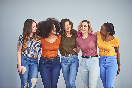 Studio shot of a group of attractive young women embracing against a gray background