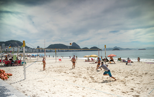 Rio de Janeiro, Brasil- March 05,2019: Men play volleyball in Copacabana. Citizens sunbathe