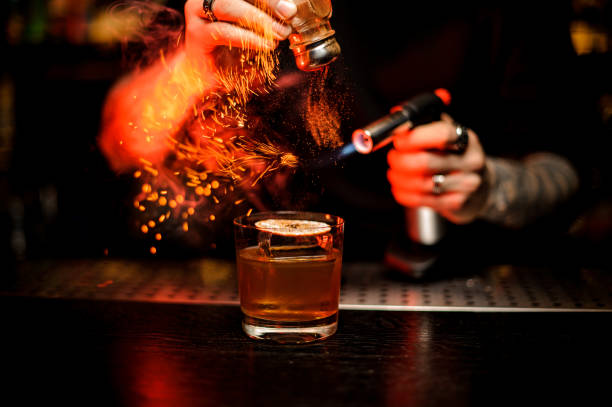 bartender adding to a cocktail spice and flame it - drink on top of ice food imagens e fotografias de stock