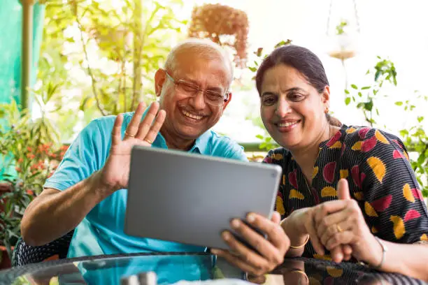 Indian/asian Senior couple video chatting on tablet/computer while sitting at couch or in garden at home, selective focus