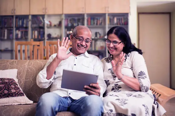 Indian/asian Senior couple video chatting on tablet/computer while sitting at couch or in garden at home, selective focus