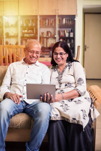 Indian/asian Senior couple video chatting on tablet/computer while sitting at couch or in garden at home, selective focus