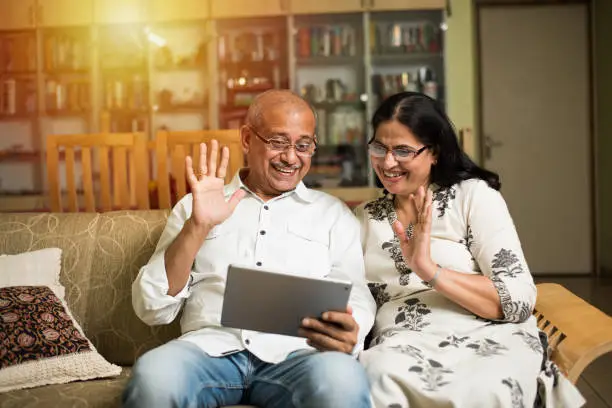 Indian/asian Senior couple video chatting on tablet/computer while sitting at couch or in garden at home, selective focus