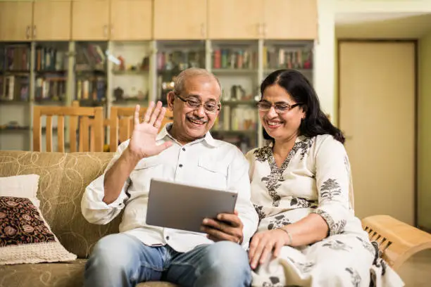 Indian/asian Senior couple video chatting on tablet/computer while sitting at couch or in garden at home, selective focus