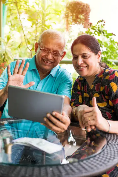 Indian/asian Senior couple video chatting on tablet/computer while sitting at couch or in garden at home, selective focus