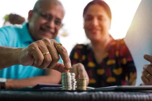 Photo of Senior Indian/asian couple arranging/staking coins pile in a row, selective focus