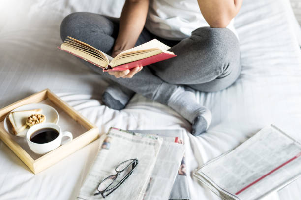 vista de alto ángulo de la mujer leyendo un libro en la cama - newspaper glasses the media reading fotografías e imágenes de stock