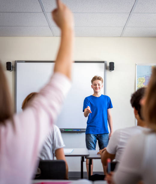 Teenage boy gesturing while giving presentation Teenage boy gesturing while giving presentation. Student is raising hand to ask doubts in classroom. Confident university student is standing against whiteboard. teenage high school girl raising hand during class stock pictures, royalty-free photos & images