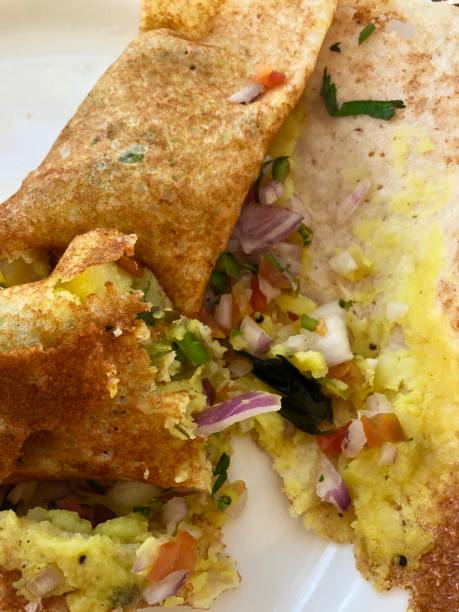 istock Image of traditional Indian breakfast at hotel restaurant buffet on white plate masala dosa / onion dosa with potato filling being eaten, green chutney, tomato and garlic dip 1137726282