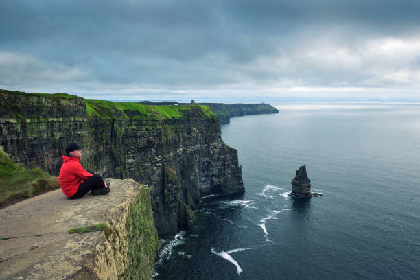 hiker sitting at the cliffs of moher - republic of ireland cliffs of moher panoramic cliff imagens e fotografias de stock