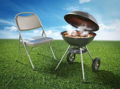 Chair and barbecue with smoking grilled meat on green grass.
