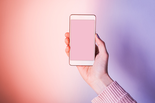 Woman's hand with mobile phone screen on pink and violet purple abstract background. Empty screen for your text.