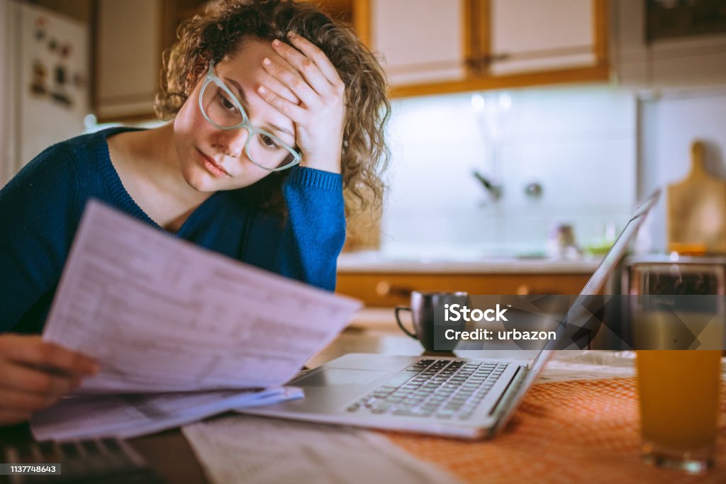 Going through documents Young female reading documents, using laptop in the kitchen at home Financial Bill Stock Photo