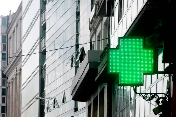 simbolo della farmacia per strada, edifici alti, croce verde. - green cross foto e immagini stock