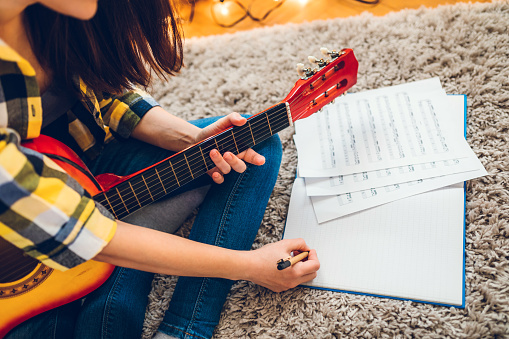 Young woman is composing a song on an acoustic guitar at home