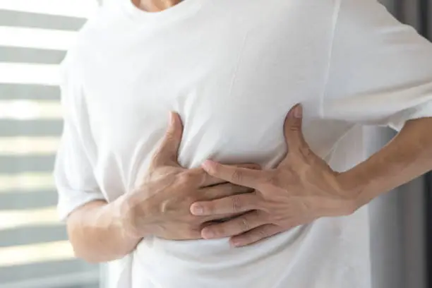 Photo of Man's hands on his chest in white shirt with red spot as suffering on chest pain. Male suffer from heart attack,Lung Problems,Myocarditis, heart burn,Pneumonia or lung abscess, pulmonary embolism day