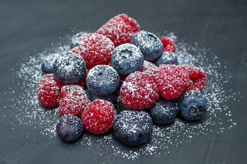 A Dusting of Icing Sugar on Blueberries and Raspberries on a Grey Slate