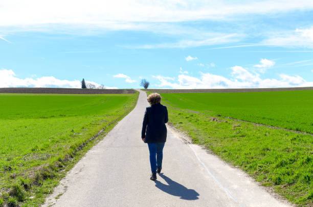 istock Woman walking away along a road through fields 1137774649