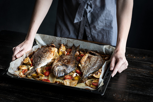 fish for dinner. in female hands baked fish on a baking sheet.