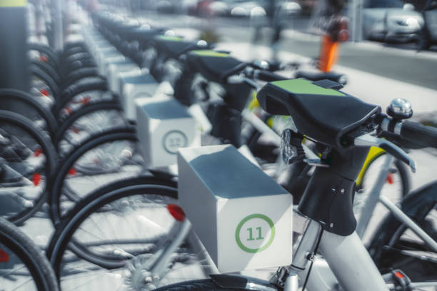 Two rows of white public electric bicycles outdoors shot with shallow depth of field; plenty of rentable city bikes with batteries on the street on a sunny day, selective focus, Lisbon, Portugal