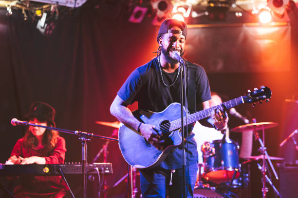 Black male guitarist singing and playing acoustic guitar on stage A black male guitarist is singing and playing the acoustic guitar on stage. performance group stock pictures, royalty-free photos & images