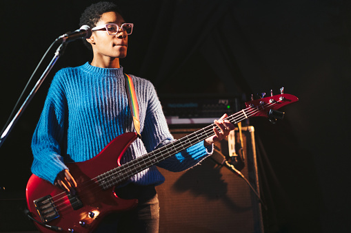 A black female guitarist is playing the bass guitar on stage.