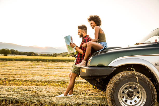 joven pareja sentada en el coche leyendo un mapa de carreteras - couple young adult african descent multi ethnic group fotografías e imágenes de stock