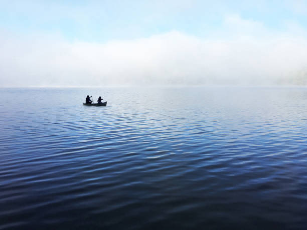Silhouette of a father and his son canoeing on a misty lake